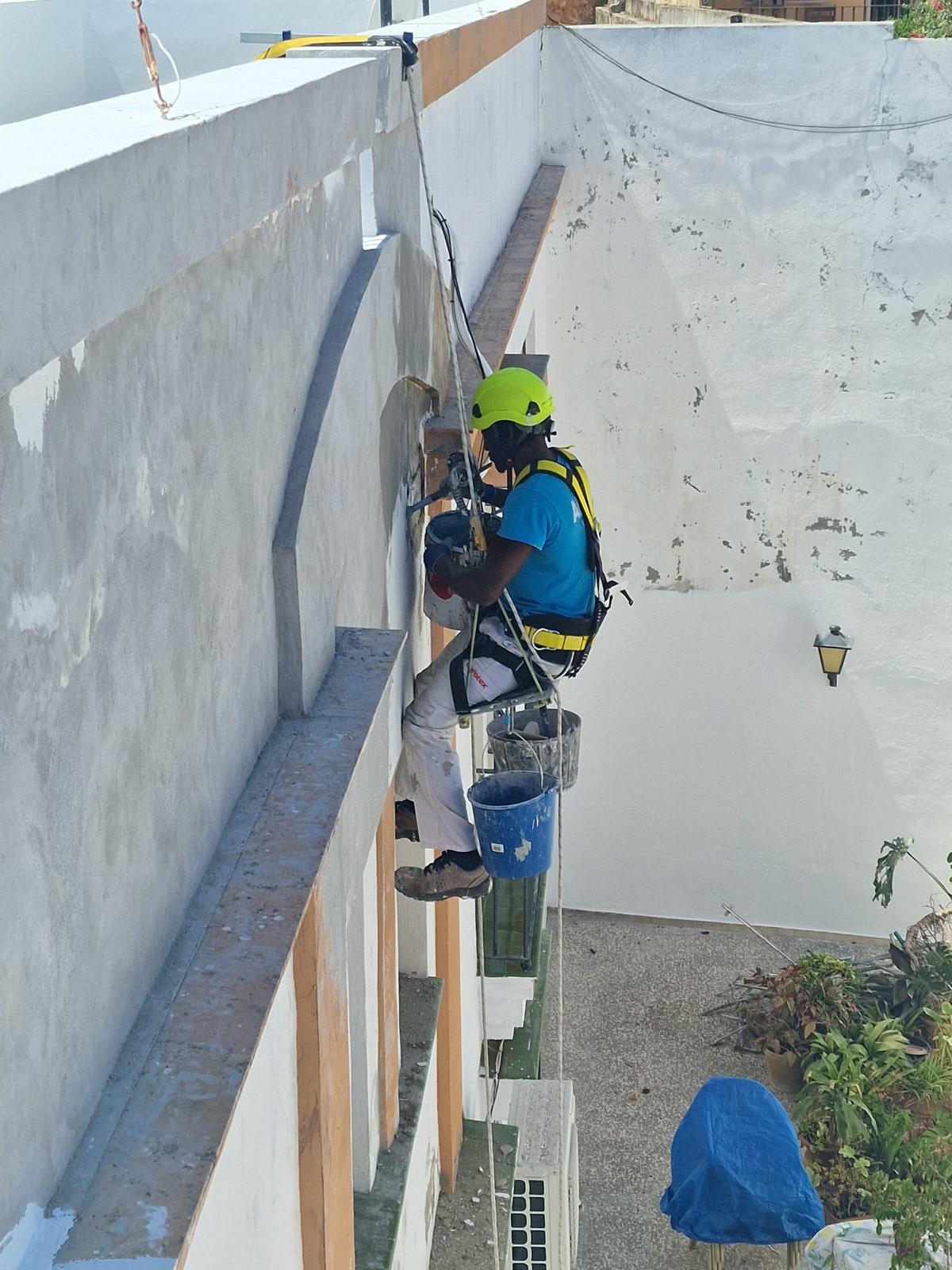 Técnico saneando y reparando el peto de una azotea con técnicas de acceso por cuerda