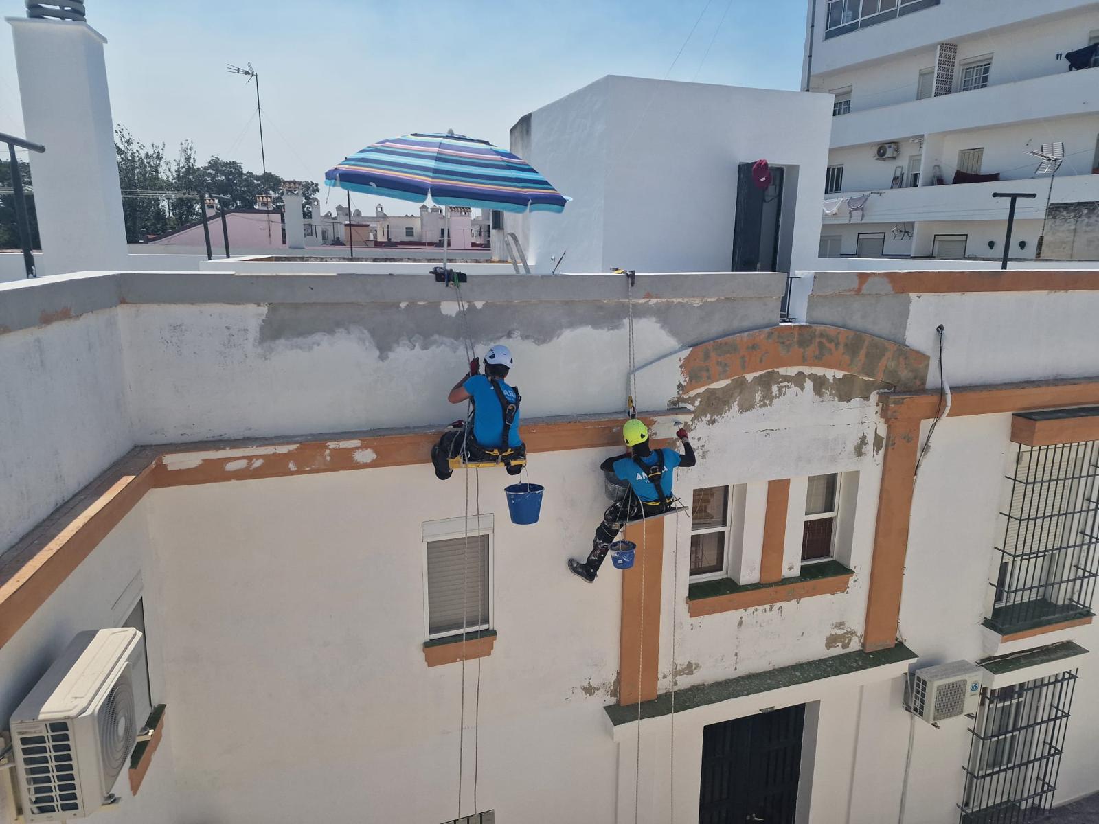 Dos técnicos suspendidos con cuerdas rehabilitando el peto y la fachada de un edificio