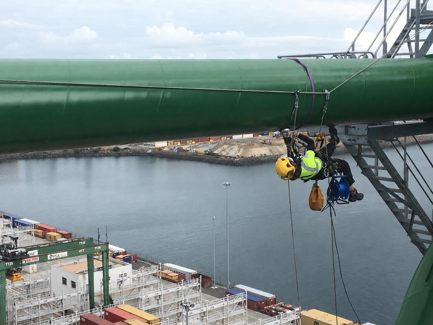 Técnico de acceso por cuerda trabajando sobre una tubería en instalaciones portuarias