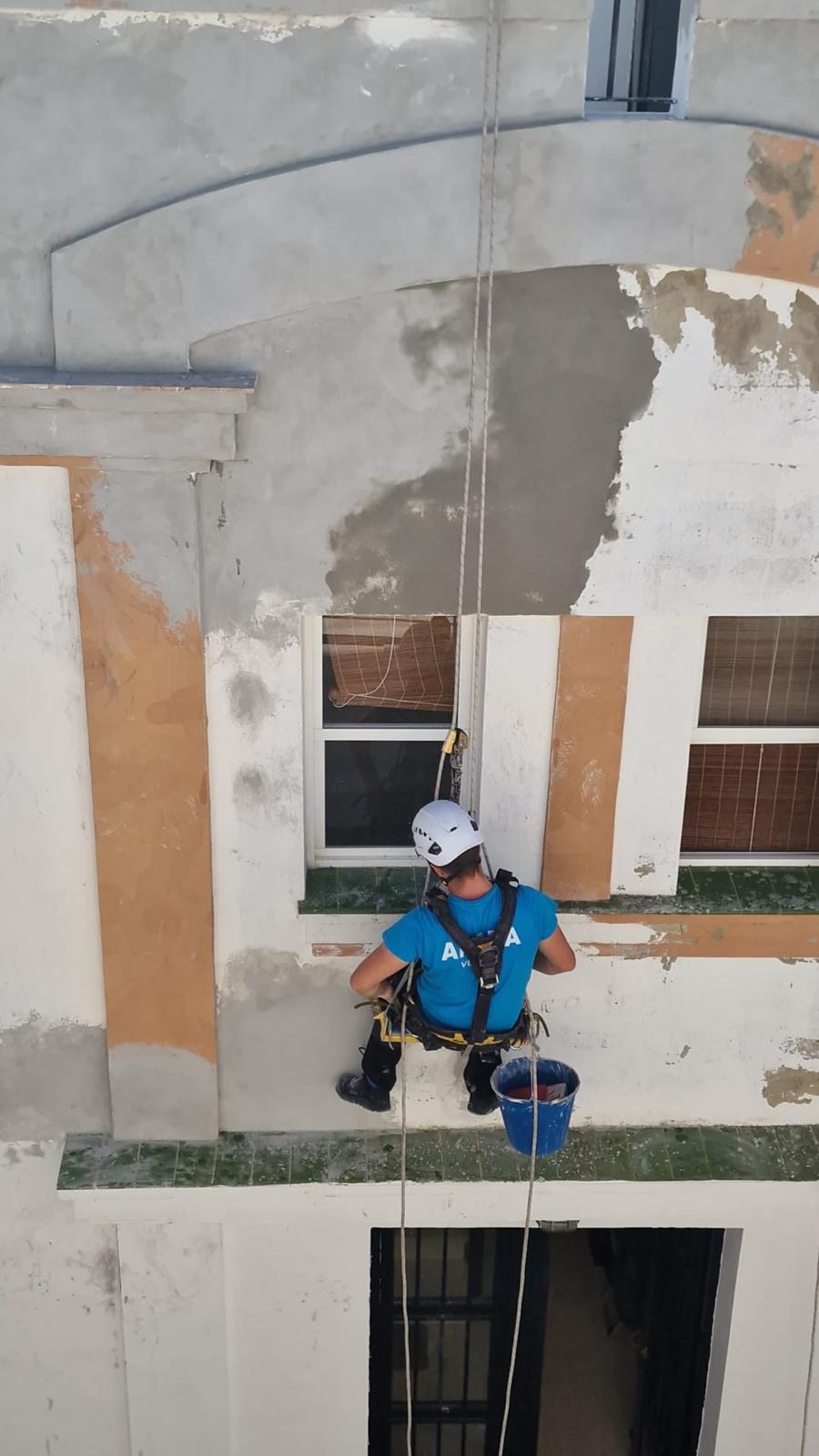 Técnico aplicando mortero en la fachada de un edificio suspendido con cuerdas