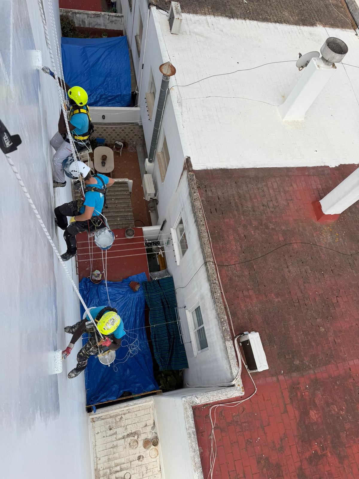 Equipo de tres técnicos pintando una fachada interior mediante trabajos verticales