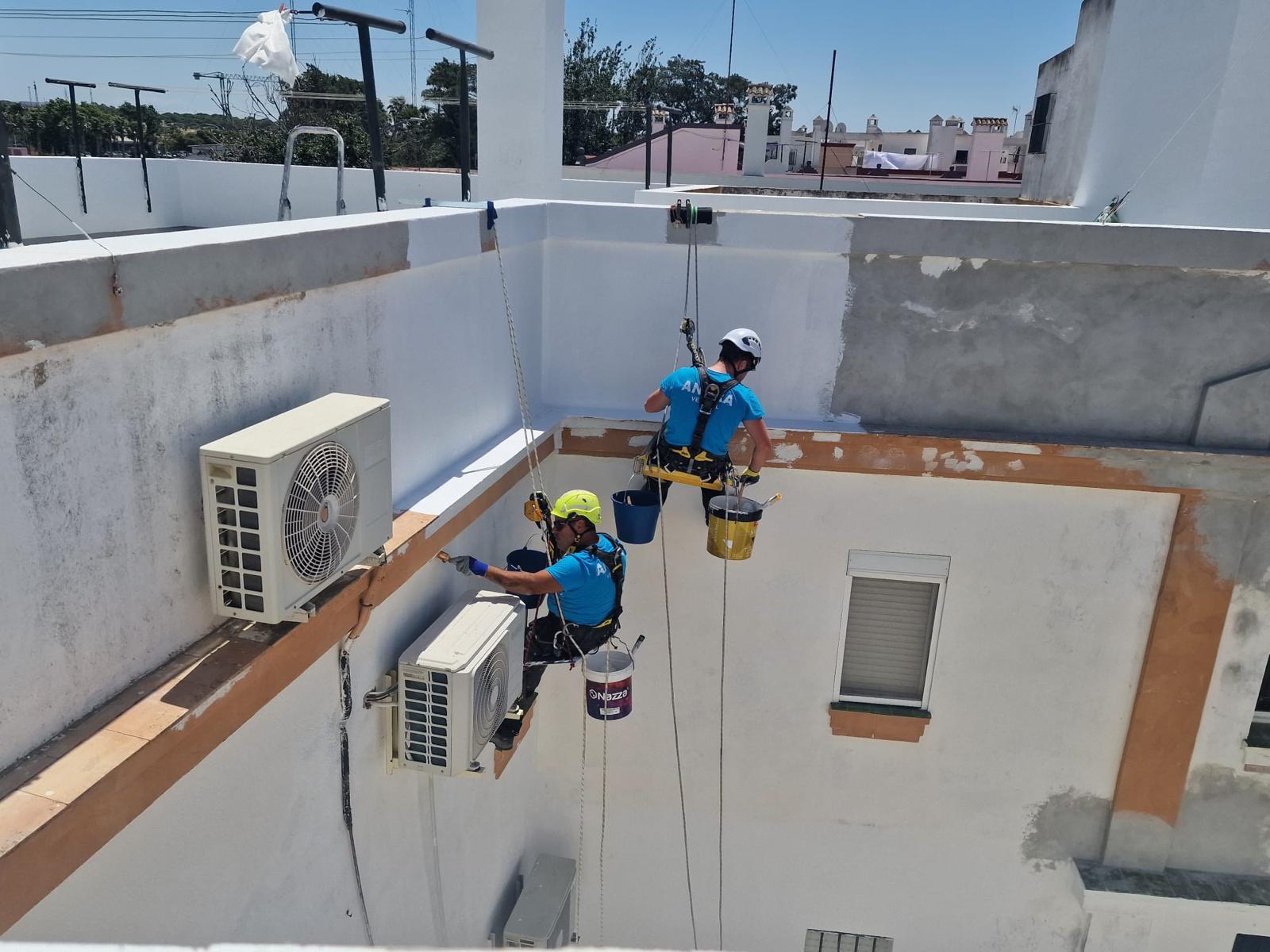 Dos técnicos de ANARA Verticales pintando la fachada de un edificio suspendidos con cuerdas